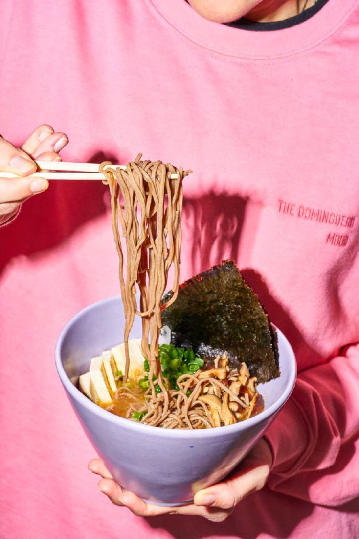 A student holding a bowl of noodles with chopsticks